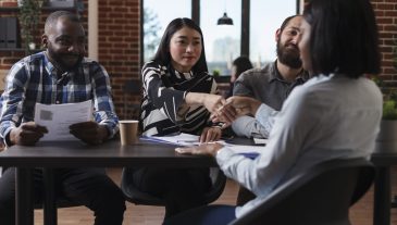 Marketing company recruiters sitting at desk in office while welcoming applicant to job interview. African american woman shaking recruitment team leader hand while making good first impression.